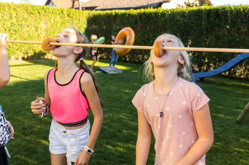 zwei Kinder beißen von Donuts, die auf einer Stange hängen
